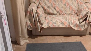 A room with a dark grey rug, a beige sofa with a patterned cover, and a white door with a keychain. - Basement Unit (Richmond Hill)