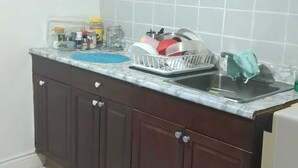 A kitchen with dark wooden cabinets, a tiled backsplash, and a countertop with a dish rack and various kitchen items. - Basement Unit (Richmond Hill)