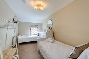 Une chambre à coucher comprenant un lit, une commode, un miroir, une fenêtre avec des stores, un radiateur et une étagère avec des articles de toilette.