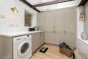 A compact laundry room with a washing machine, cabinets, a clock, and a small window.