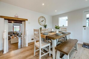 A dining area with a wooden table set for four, white chairs, and a clock on the wall. - 3 Bed in West Down (oc-r29627) (West Down)