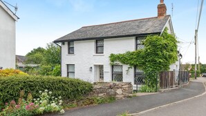 A white two-story house with a stone foundation, a tiled roof, and a garden with various plants and flowers. - 3 Bed in West Down (oc-r29627) (West Down)