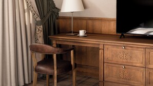 A hotel room with a wooden desk, a television, a lamp, a chair, and a plaid-patterned carpet. - Willa na Kozińcu (Zakopane)