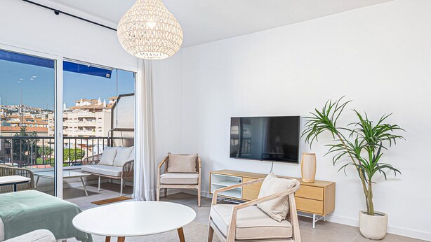A modern living room with a balcony, a flat-screen TV, a wooden desk, and a potted plant. - Ida - Rental in Rincon de la Victoria (Rincón de la Victoria)
