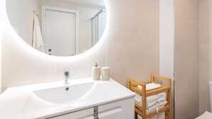 A bathroom with a round mirror, white sink, and a wooden towel rack. - Ida - Rental in Rincon de la Victoria (Rincón de la Victoria)