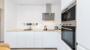 A modern kitchen with white cabinetry, a stainless steel range hood, a kettle, a coffee maker, and a built-in oven. - Ida - Rental in Rincon de la Victoria (Rincón de la Victoria)