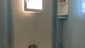 Ein Badezimmer mit Badewanne, einem Fenster und einem Ablagefach mit Pflegeprodukten.