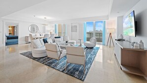 A spacious living room with a large sofa set, a coffee table, and a TV mounted on the wall. - Ritz-Carlton Luxury - Oceanfront 2BR on 16th Fl (Fort Lauderdale)