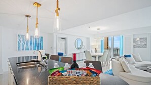 A modern kitchen with a large island, dining area with white chairs, and a living area with a sofa and a coffee table. - Ritz-Carlton Luxury - Oceanfront 2BR on 16th Fl (Fort Lauderdale)