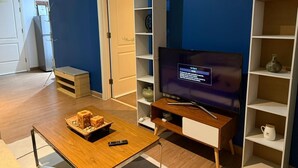 A living room with a television, wooden coffee table, and shelves. - One Bedroom with Balcony City view  (Makati)