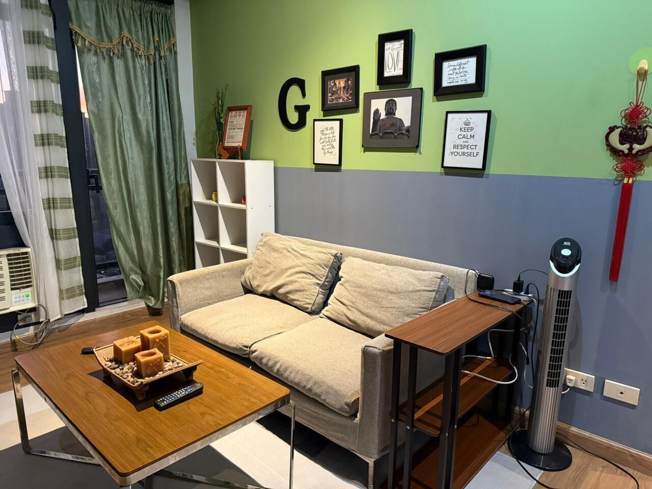 A living room with a sofa, a coffee table with candles, and a wall with framed pictures and a letter 'G'.