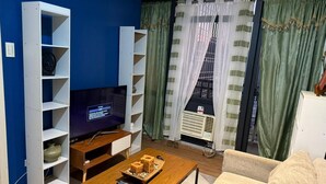 A living room with a flat-screen TV, a wooden coffee table with items, a beige sofa, and a white entertainment unit. - One Bedroom with Balcony City view  (Makati)