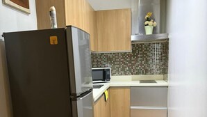 A compact kitchen with a stainless steel refrigerator, a microwave, wooden cabinets, a tiled backsplash, and a small trash bin. - One Bedroom with Balcony City view  (Makati)