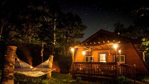 Una cabaña de madera con un porche, una hamaca y un cielo nocturno lleno de estrellas.