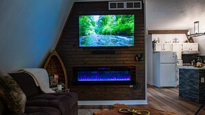Una sala de estar con televisor, chimenea y zona de cocina.