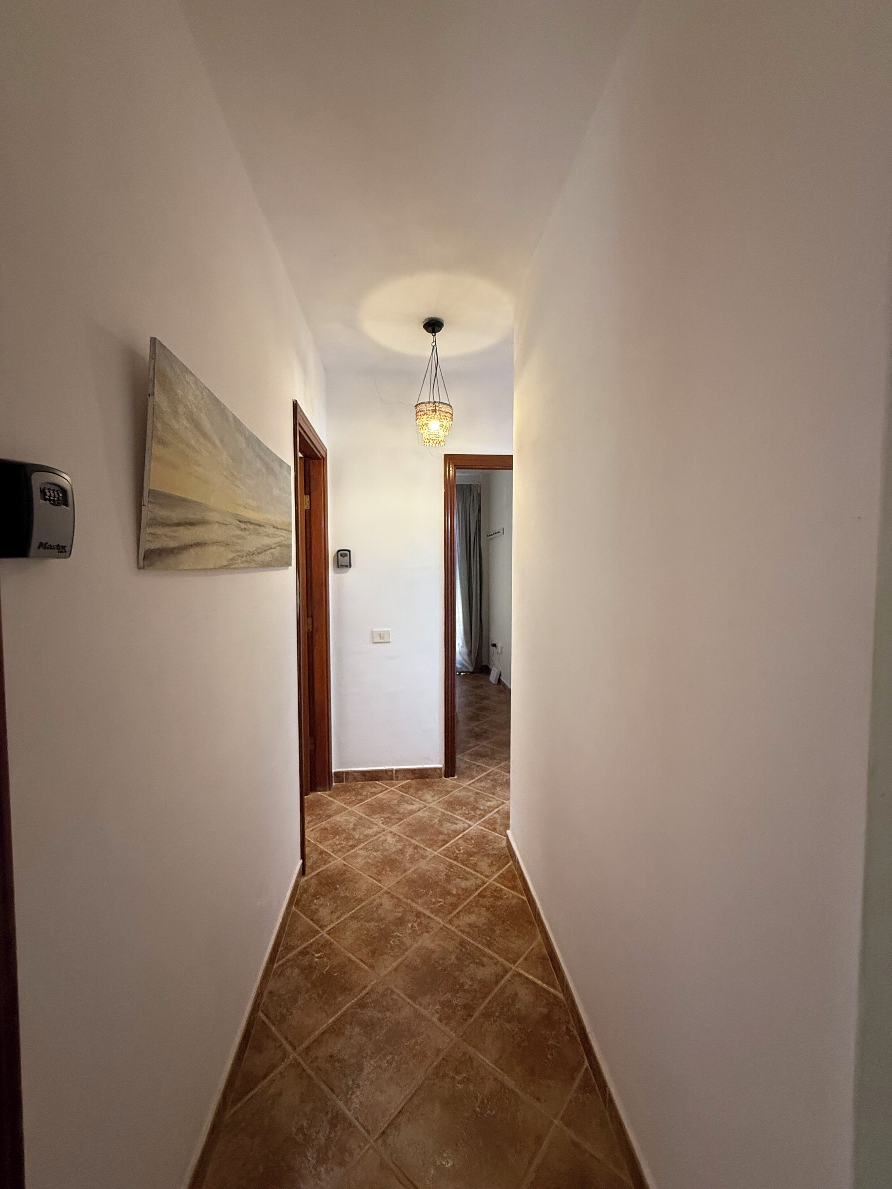 Un pasillo con suelo de baldosas, un cuadro en la pared izquierda y una lámpara en el techo.