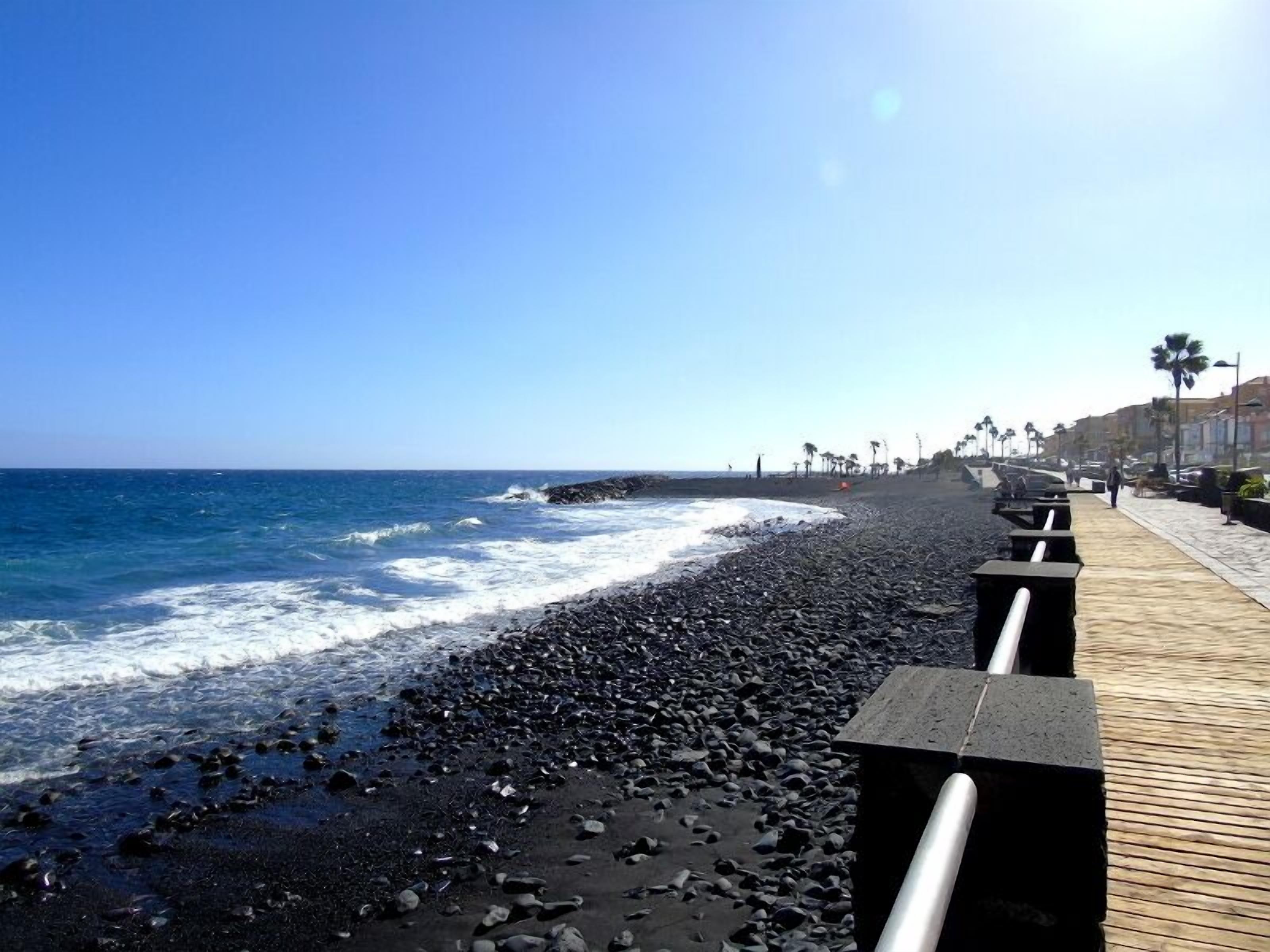 A beach with a wooden walkway, ocean waves, and palm trees.