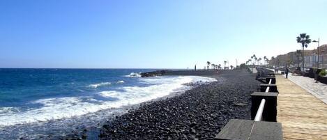 A beach with a wooden walkway, ocean waves, and palm trees.