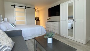 Ein modernes Hotelzimmer mit Bett, Sofa, Fernseher, Kleiderschrank und einer kleinen Küchenzeile.