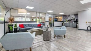 Ein moderner Lounge-Bereich mit einer Couch, Sesseln, einer Kaffeebar und Blick auf die Küche.