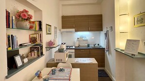 Una cucina compatta con mobili in legno, una zona pranzo con tavolo apparecchiato per due e una libreria con diversi oggetti.
