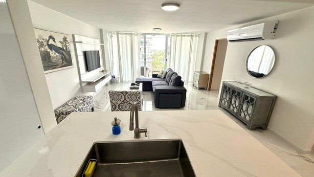 A modern living room with a sofa, a TV, a dining area, and a kitchen with a sink.