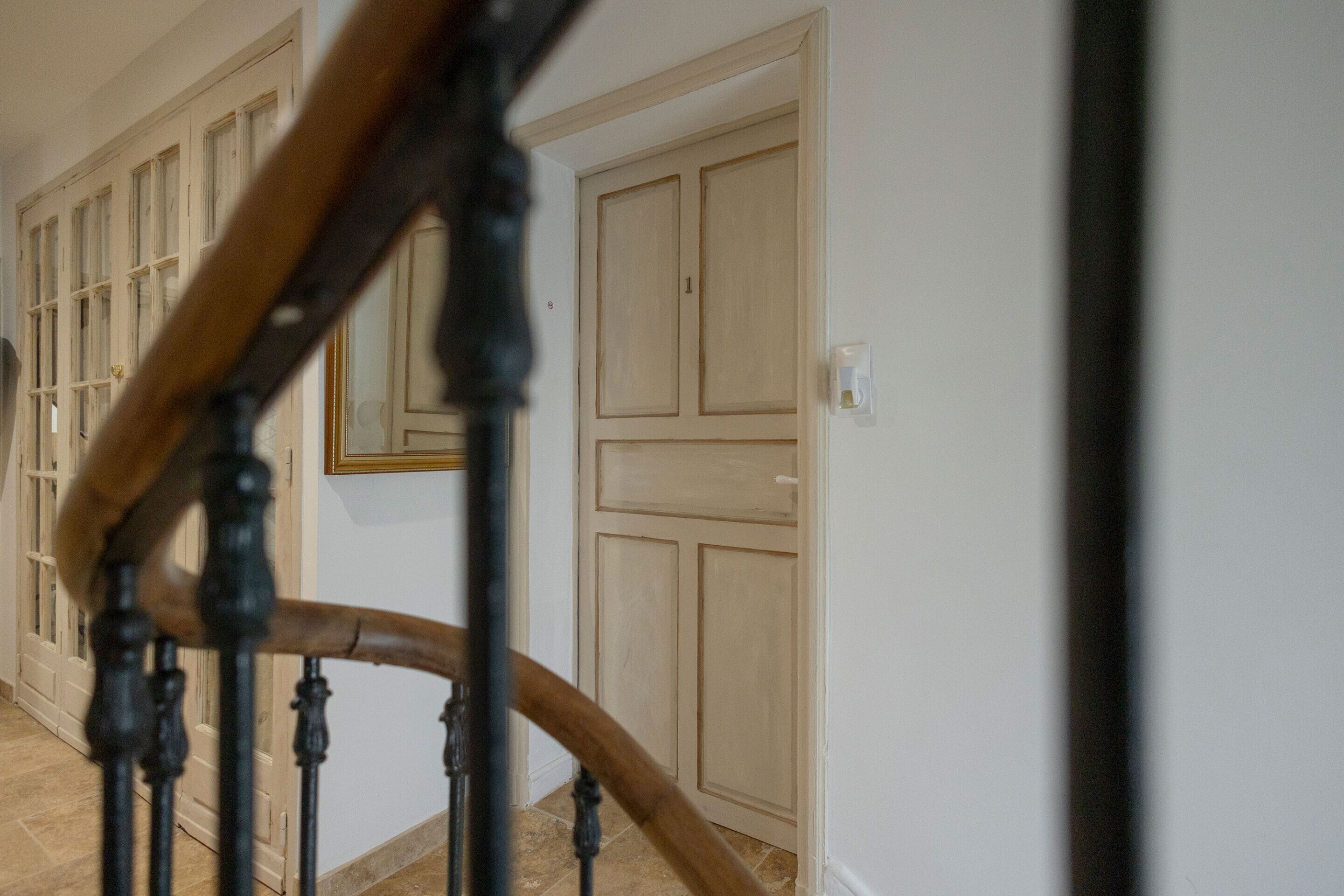 Un escalier en bois, doté d’une rampe, mène à une porte sur laquelle est apposé le numéro « 1 ».