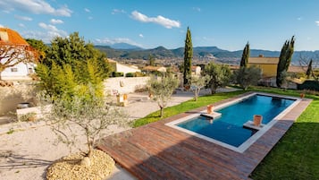 Una piscina rectangular con un deck de madera, rodeada por un césped cuidado y árboles.