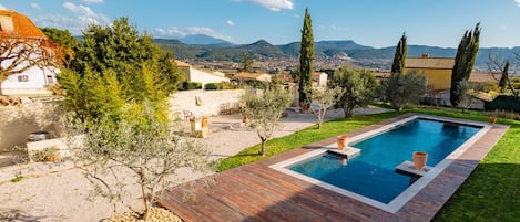A rectangular swimming pool with a wooden deck, surrounded by a well-maintained lawn and trees.