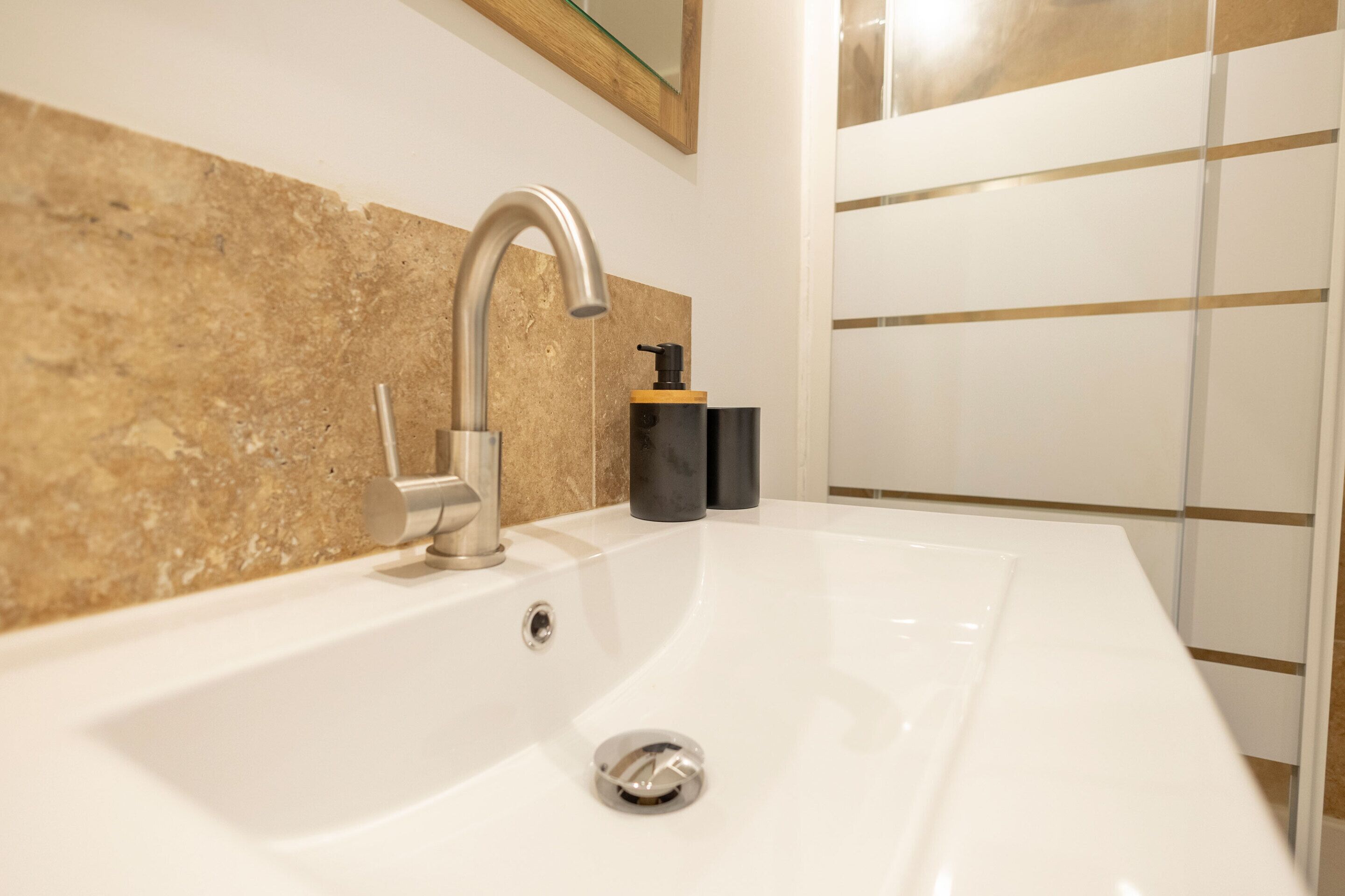 A modern bathroom with a white sink, a curved faucet, and a beige tiled wall.