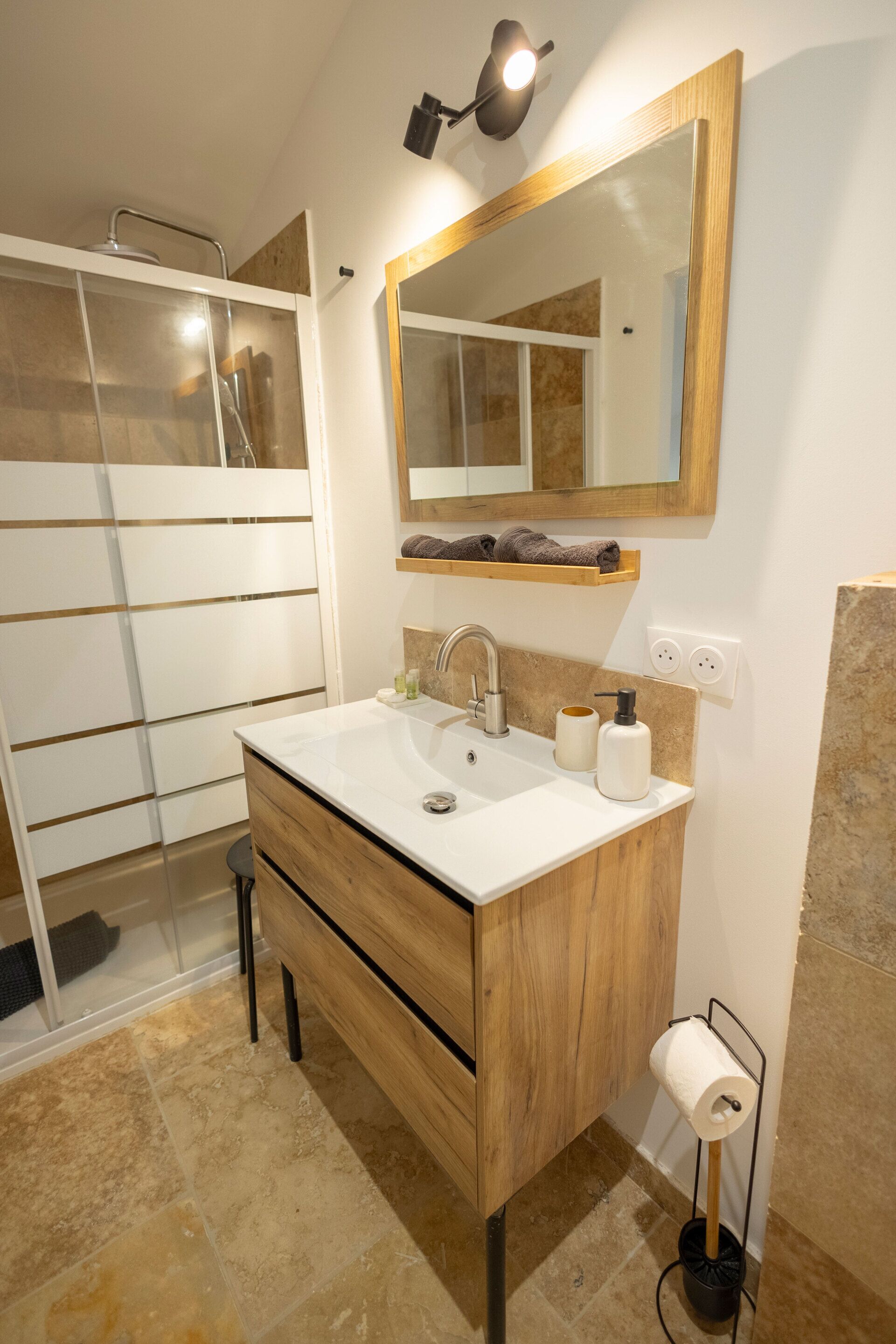 A modern bathroom with a wooden vanity, a glass shower enclosure, and a mirror above the sink.
