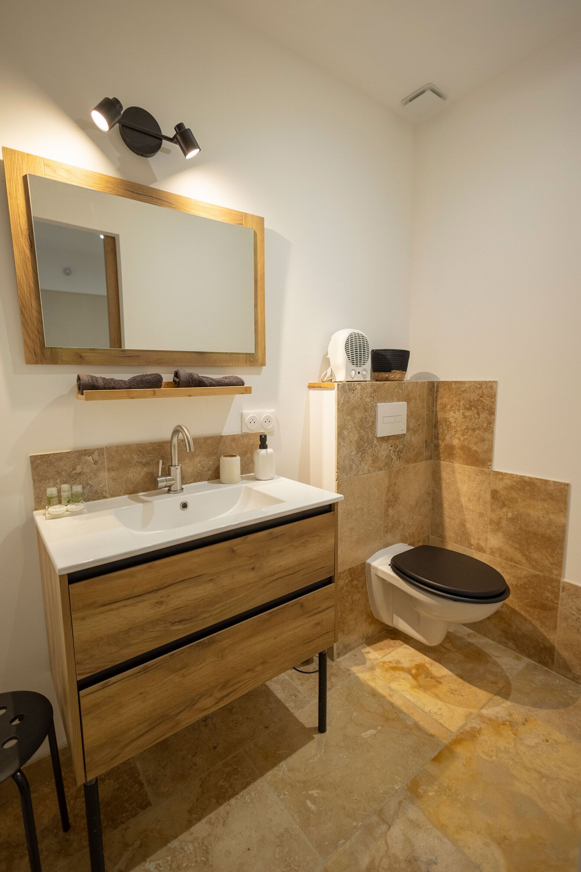 A modern bathroom with a wooden vanity, a large mirror, a white sink, and a toilet.
