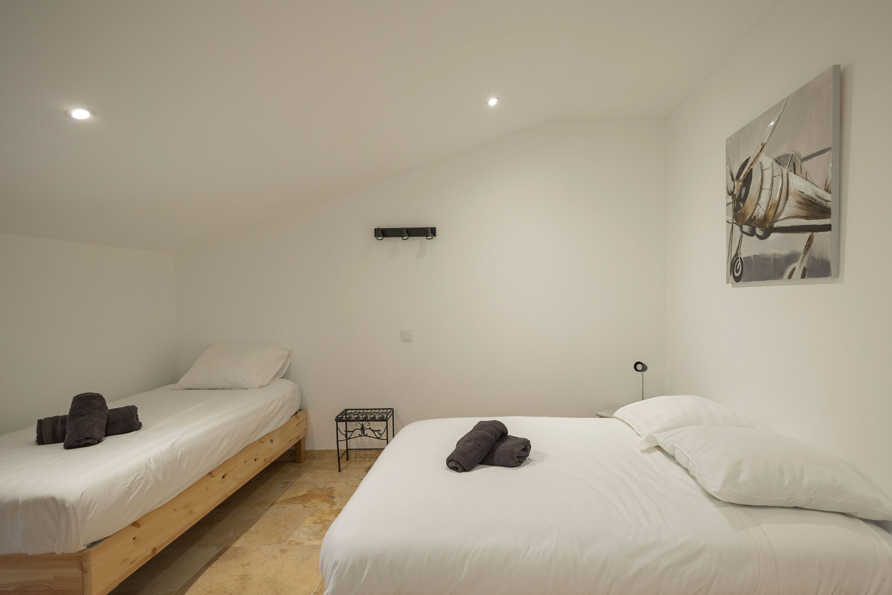 Een slaapkamer met twee enkele bedden, een klein tafeltje en een wandlamp.