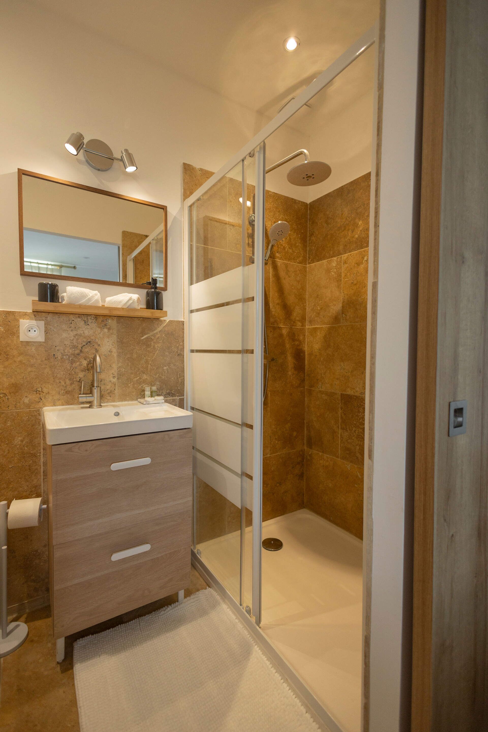 Un baño moderno con cabina de ducha de vidrio, tocador con lavabo y espejo sobre el tocador.
