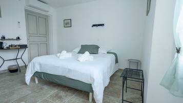 Quarto bem arrumado com cama, mesa de cabeceira e um banquinho.