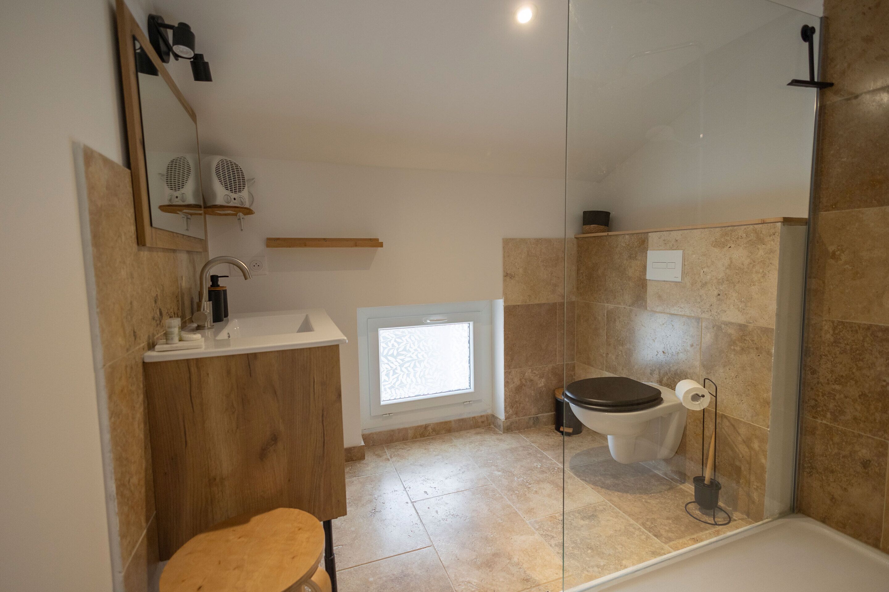 Et moderne badeværelse med en trækommode, toilet, brusebad og et lille vindue.