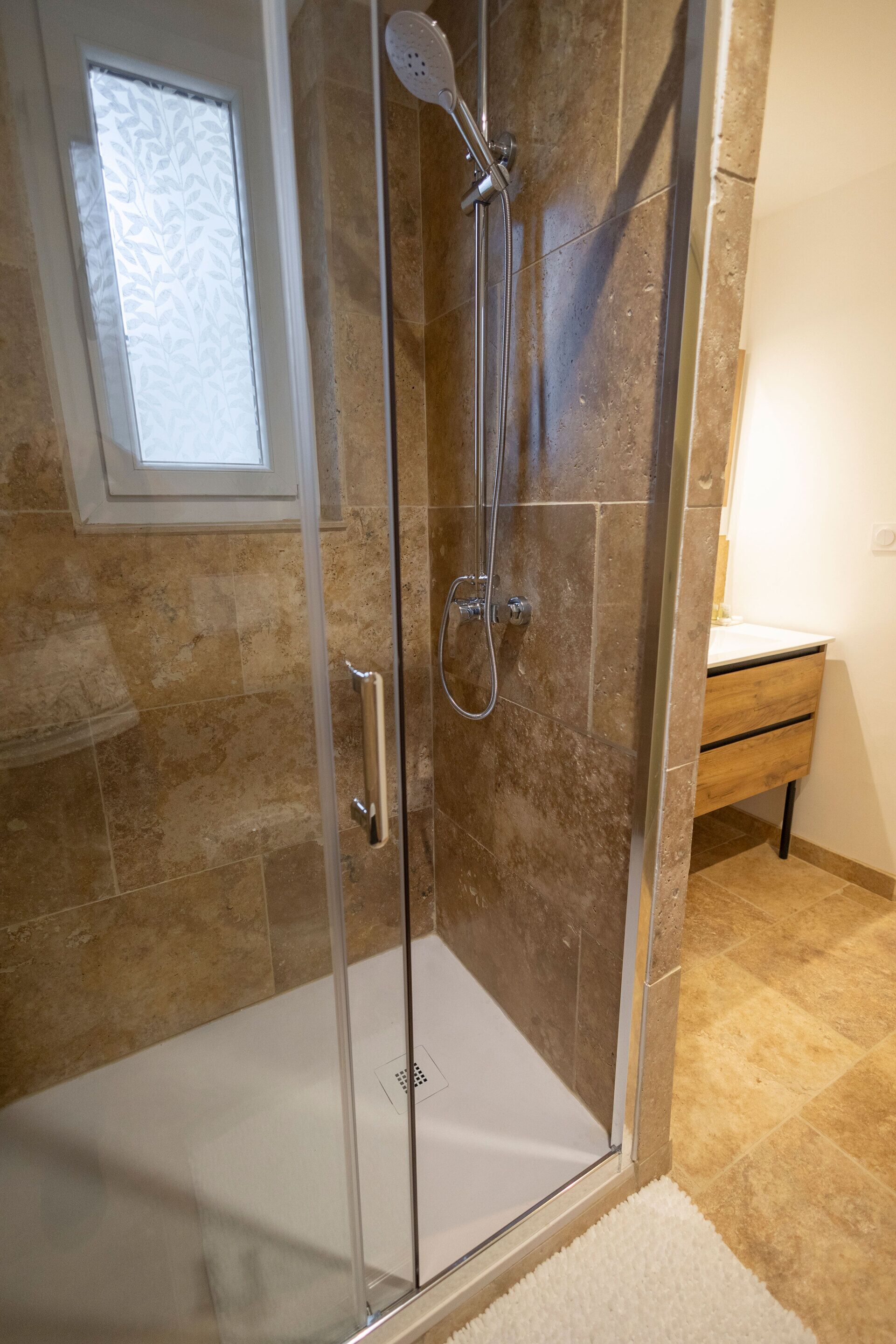 Ducha envuelta en vidrio, con cabezal de ducha de mano y llave de pared.