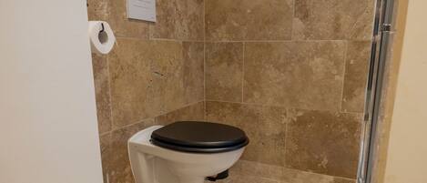 A bathroom with a toilet, a white rug, and a shower area.