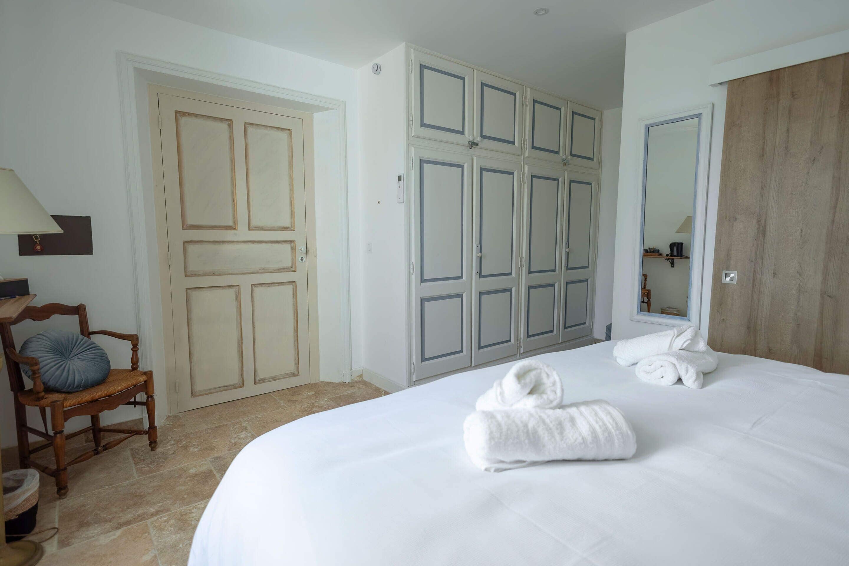 A hotel room with a large bed, a wooden wardrobe, a chair, and a mirror.