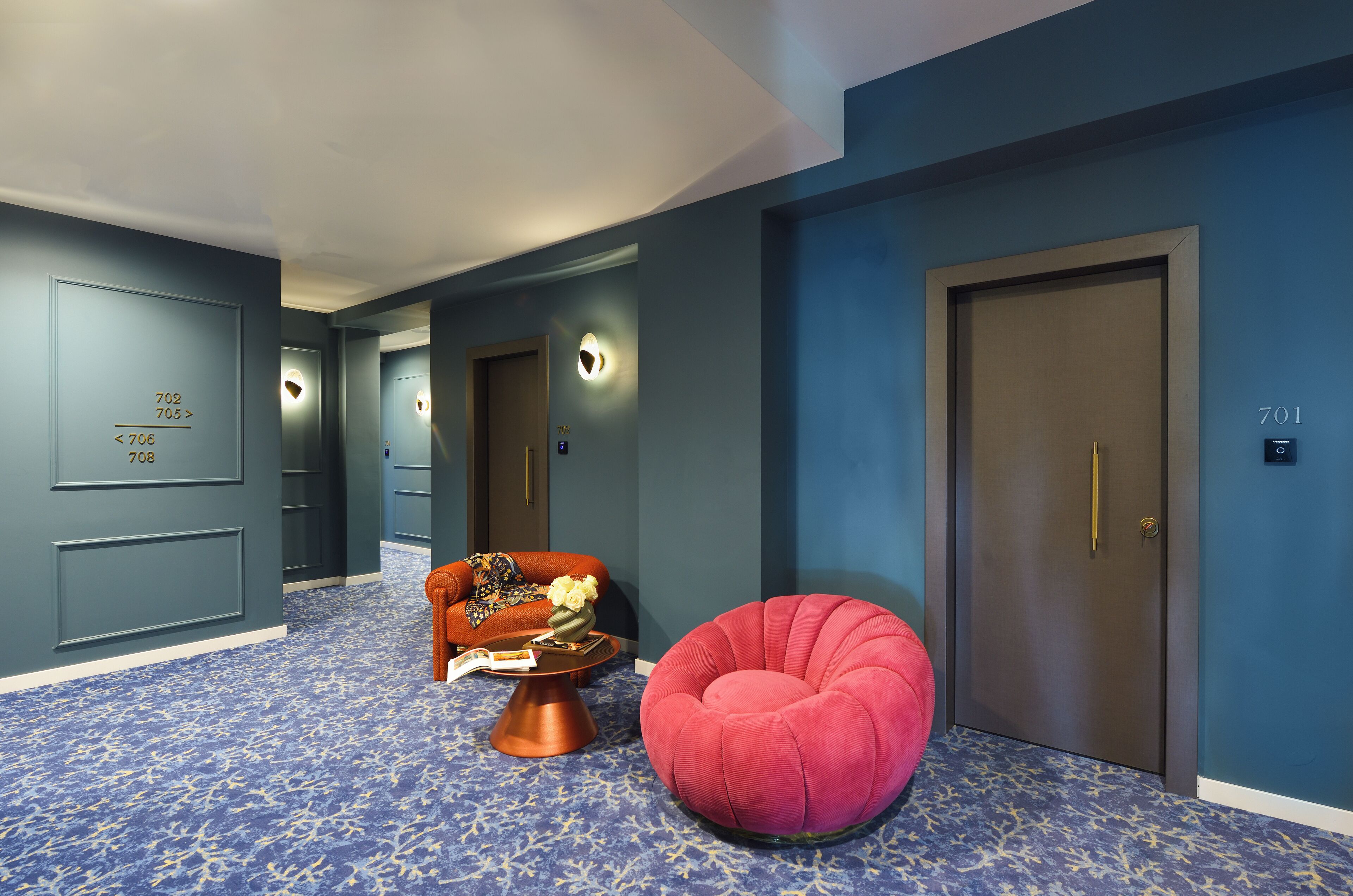 A hallway with a blue carpet, a red chair, a brown sofa, and a door marked with the number 701.