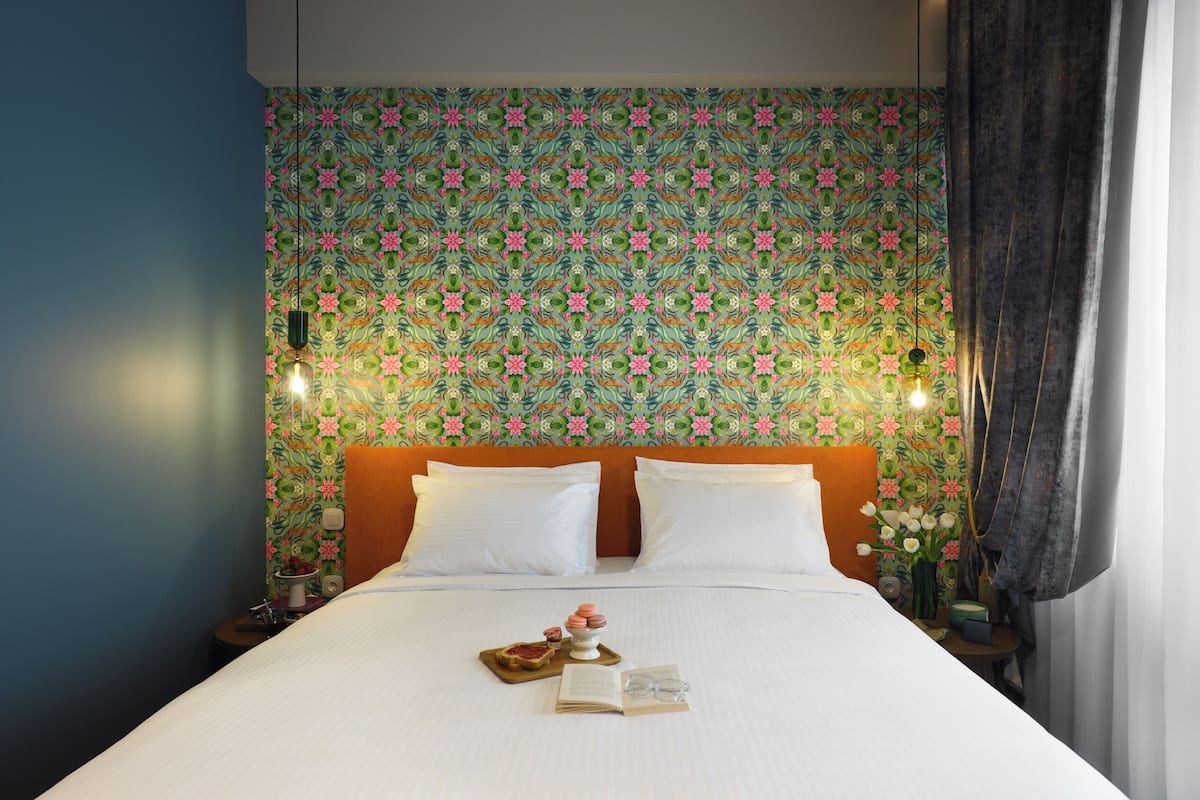 A neatly made bed with white linens, a floral-patterned headboard, and a tray with pastries and a book.