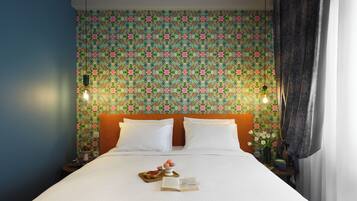 A neatly made bed with white linens, a floral-patterned headboard, and a tray with pastries and a book.