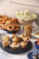 A table with pastries and baked goods, including muffins and donut holes, and a bowl of flowers.