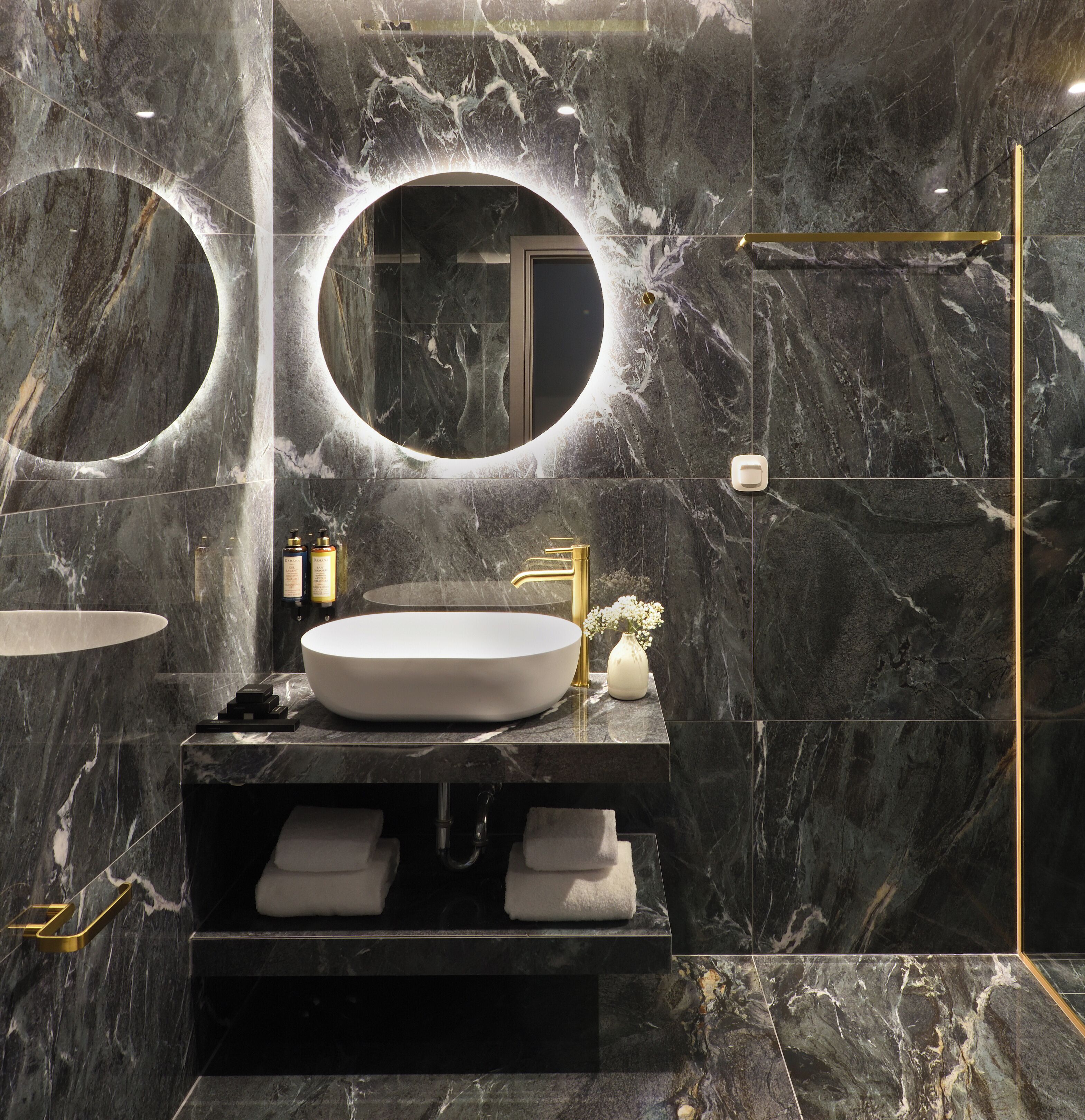 Un baño moderno con un lavamanos ovalado grande, dos espejos redondos y un grifo dorado.