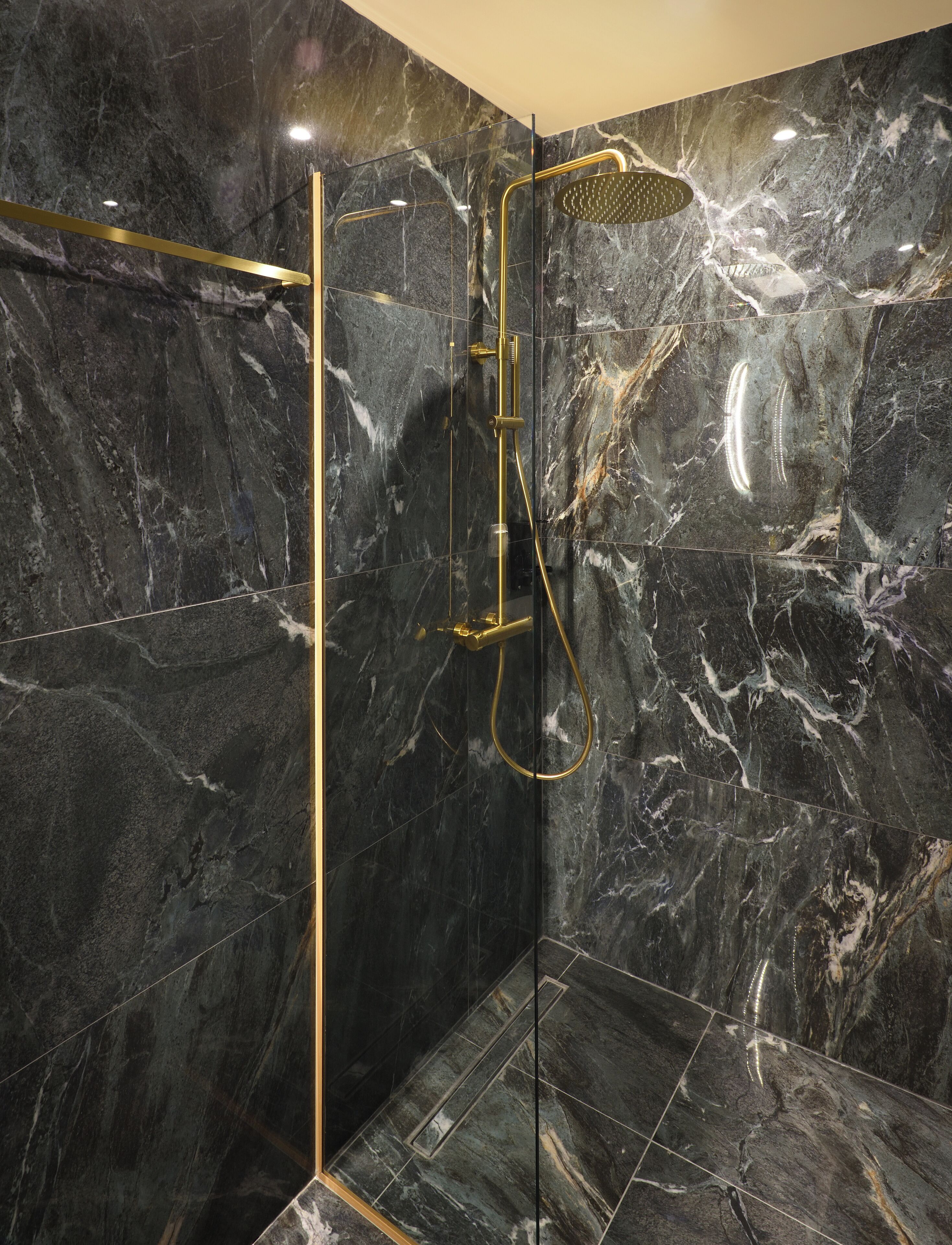 A modern bathroom with a black marble wall, a gold shower head, and a glass-enclosed shower area.