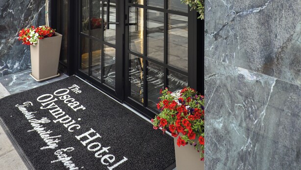 The entrance to The Oscar Olympic Hotel with a marble facade, a black door, and a welcome mat. - The Oscar Olympic Hotel (Thessaloniki)