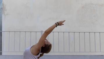 A person performing a yoga pose on a pink mat in an outdoor setting with a checkered floor and a plain wall in the background.