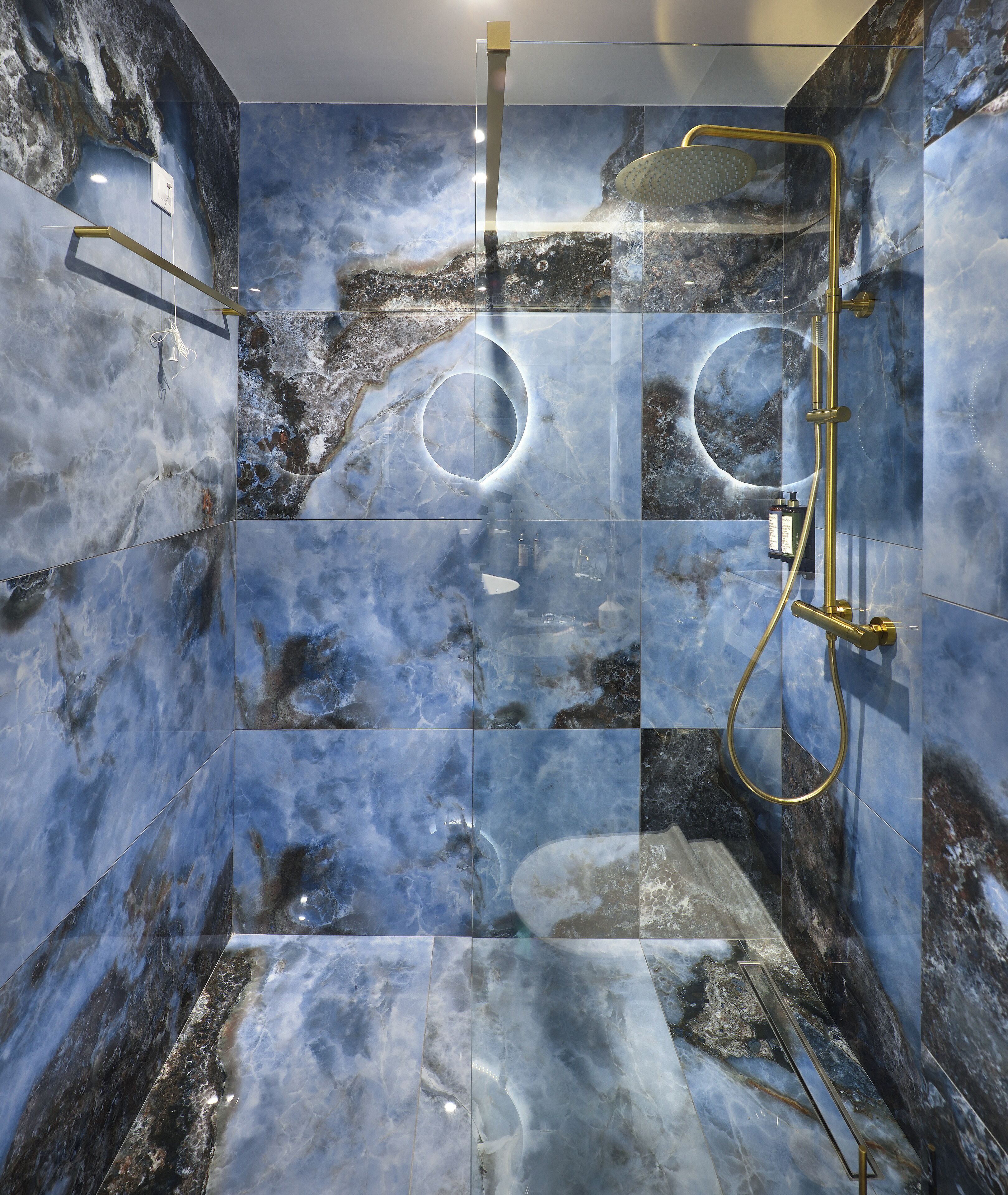 Une douche moderne avec un pare-douche en verre, des murs en marbre et des accessoires dorés.