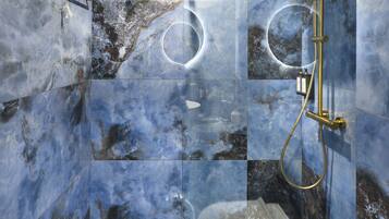 Une douche moderne avec un pare-douche en verre, des murs en marbre et des accessoires dorés.