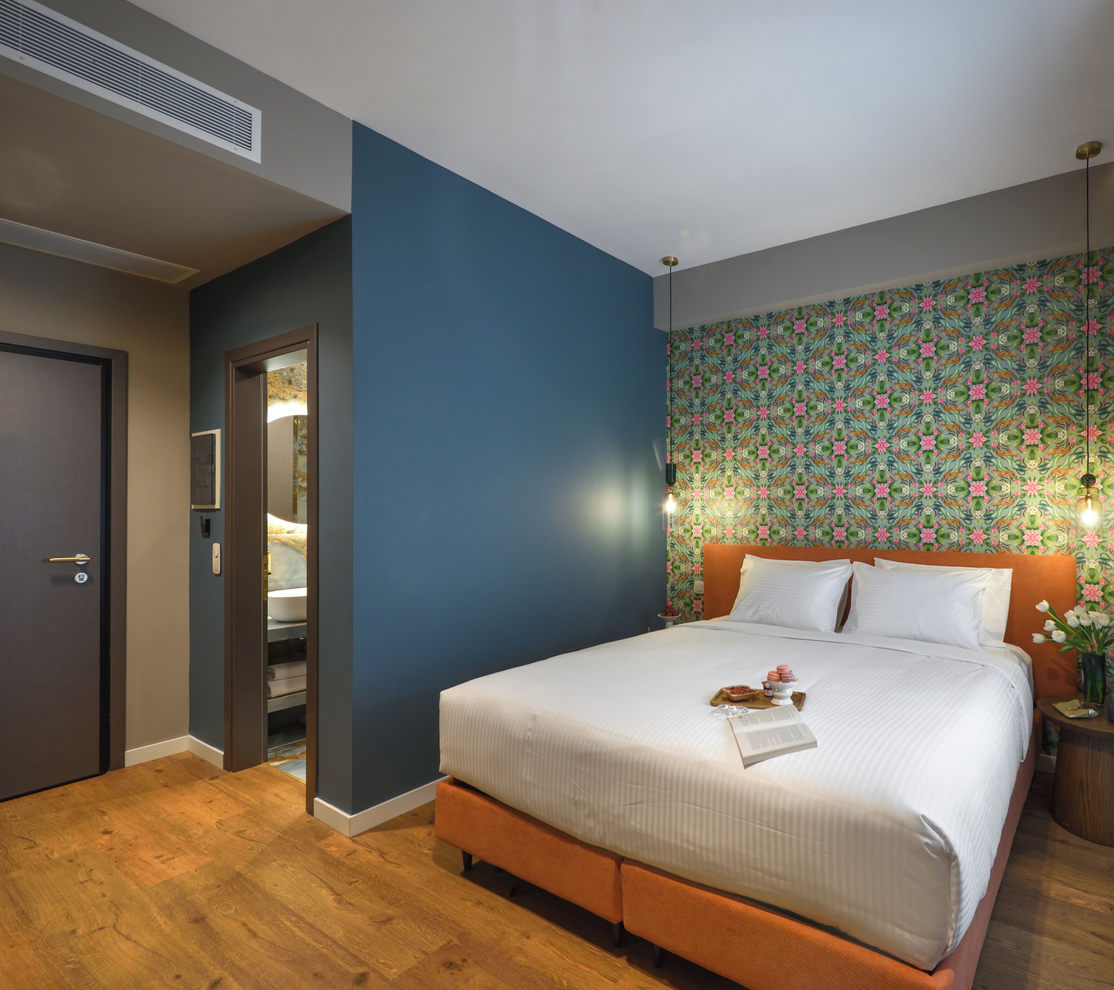 Moderni hotellihuone, jossa on suuri sänky, puulattia, sininen tehosteseinä ja kukkakuviollinen tapetti.
